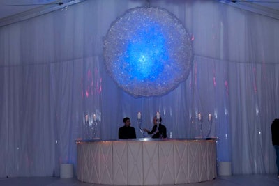 At the back of the tent, a glowing, spherical chandelier made of plastic hung above a white, semicircular bar.