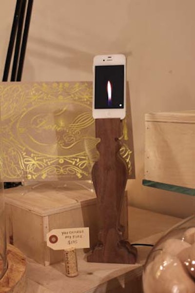 A wooden candlestick has a phone charger at its top; placing an iPhone that displays a candle flame app on it results in a contemporary tabletop design idea.