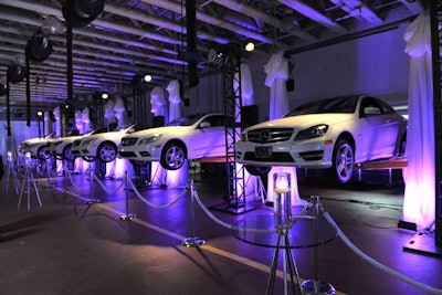 White Mercedes-Benz vehicles, suspended by car lifts, lined the cocktail space. Westbury uplit the area with purple lights.