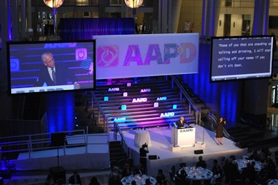 The three projection screens making up the stage backdrop showcased the speakers, a color-changing version of the organization's redesigned logo, and transcription of the speakers for the hearing-impaired guests.
