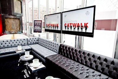 Black and white lounge furniture from Divine fills the dedicated reception space. Two screens display marketing images for Fashion Week.