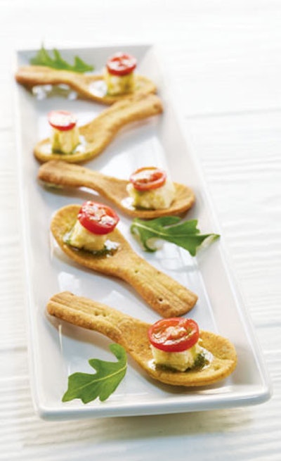 Leek cheesecake with arugula pesto, caramelized onions, and a sweet grape tomato served in a pesto cracker spoon, by Puff ’n Stuff Catering in Orlando