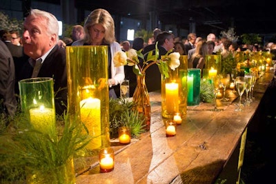 In the center of the reception space, a reclaimed wood and cinder block communal table was surrounded by wooden stools and topped with tree peonies and candles in clear green and yellow-hued vases. The space beneath the table was filled with more greens, including Italian ruscus, Pangola grass, and Johnson grass.