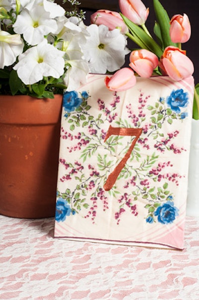 LoLo Event Design offers hand-painted handkerchiefs that can serve as table numbers at a garden event. Geraniums in a terra cotta pot have a more casual feel than an elaborate formal centerpiece.