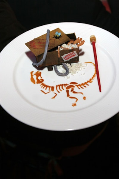 For dessert at the recent Give Kids the World gala, the Peabody Orlando served a handcrafted chocolate 'crate' filled with layers of chocolate mousse and Arabica coffee crème brûlée, accompanied by a wild cherry praline wafer and almond cookie 'fossils' sitting in pistachio dust. The dessert was presented on a plate with a hand-screened image of a dinosaur, along with a chocolate rope, edible stamps, and a chocolate dusting brush.