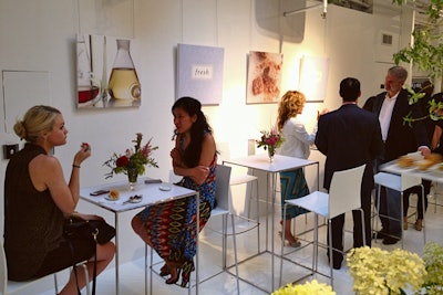 Raising tables and chairs stood near the open kitchen, allowing guests to it and sample the prepared foods. Brand signage and atmospheric imagery peppered the walls as decoration.