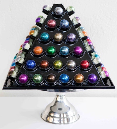 Bedazzle My Bonbons is offering a new display option. The Bonbon Pyramid displays 84 glitter-coated chocolates on all four sides. The pyramid can be placed on a lazy Susan to create a rotating display, and it folds flat when not in use. The pyramid costs $50, plus $1.50 per bonbon. The bonbons come in six flavors: original, extra dark, raspberry, hazelnut, peanut butter, and mint. The edible glitter coating comes in 24 shades, or can be custom made to match decor.