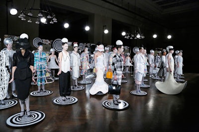 Thom Browne returned to the New York Public Library's Edna Barnes Salomon Room, this time bringing a conceptual presentation to the space. The September 10 outing produced by Villa Eugenie featured models with hair coiled into buns teased high atop their heads. Models took their positions from disc-shaped platforms and were spun in place by male 'ushers' clad in gray seersucker suits.