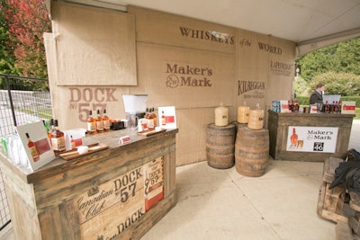 The whiskey tent was open on three sides, and, to hide the backs of the bars without closing off the area, Wagner employed a wood-slat design that framed the front corners of the space. She also designed a burlap backdrop with stenciled brand names and brought in distressed bars and barrels. The overall look, Wagner said, had a 'woodsy distillery feel.'