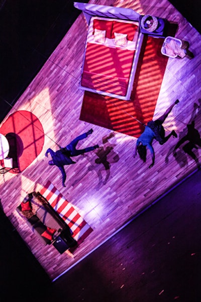 An on-stage aerial performance was announced via a kabuki drop of a red curtain that revealed a 32- by 20-foot vertical wall, designed to depict an apartment on its side. Featuring furniture available at Target, aerialists ran, danced, and flipped across the pieces, which were all attached with bolts and had straps hidden within allowing the dancers to grab and secure their footing.