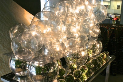 Broadway Gourmet Caterers' Winter Frolic package displays snacks on reflective white and blue tables that can be set up at offices or event spaces. One of the tables, called the Bubble Bar, uses clear, round ornaments to hold individual winter squash, pear-arugula, and winter farro salads. The salads are set against a backdrop of clear beach balls.