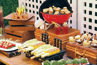 Grilled corn on the cob with assorted toppings; roasted potato salad on chive sticks; watermelon cubes with feta and spinach; spinach salad with chopped eggs and microgreens in bacon cups; “hot dog” and “hamburger” macarons; and apple pie parfaits, by Windows Catering Company in Washington