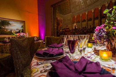 Each place setting had purple napkins atop blue chargers and white linens with a purple, orange, and lime-green geometric pattern. The short centerpieces incorporated the same colors with the addition of pink to further brighten up the table in the darker room. Moss-green chair covers and lime-green votive candles completed the look.