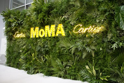 The arrivals backdrop—featuring the Cartier and MoMA logos rendered in neon and marquee lights—echoed the dense arrangements of tropical greenery found inside the dinner space.