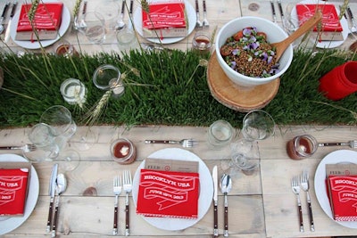 On the wooden farm tables, Hatch Creative Studio punctuated wheatgrass flats with wheat stocks and red Mason jars holding candles. Custom red bandannas printed with event details served as napkins, and family-style bowls of pickled beet, wheat berry, and kale salads sat atop platforms made from tree trunks.