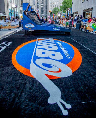 In the plaza, five Skee-Ball machines stood on a platform covered with a branded carpet. Nearby pit crews used radios to communicate with riggers atop the building, notifying them as each player scored points on the arcade games.