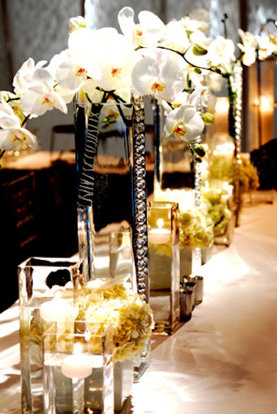 'A modern spin on traditional orchids—wire-wrapped phalaenopsis bouquet clusters inside glass vases strung with hints of chandelier crystal chains, down long banquet tables.'