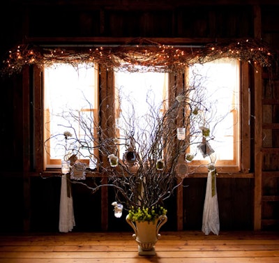 Set up inside a rustic New England barn, an escort card tree made with branches, mirrors, and moss held hand-lettered kraft paper envelopes, secured with tiny clothespins.