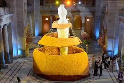 In the center of the Great Hall, a 30-foot-high oversize replica of Charles James's sculpture of an idealized female form was covered in white roses. Encircling it was a half-made gown composed of brass bars and gold roses. The enormous installation rose above the Great Hall's information desk, which was surrounded in dusty brown roses.