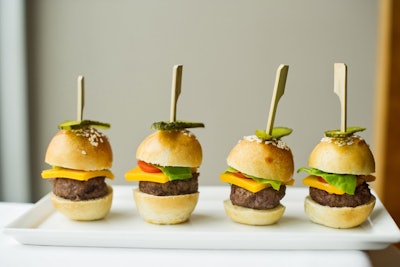 Miniature beef burgers, topped with melted cheddar cheese, dill pickles, and butter lettuce, on petite sesame-seed brioche buns, by L-Eat Catering in Toronto