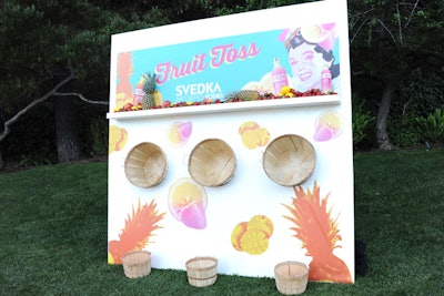 A “fruit toss” game let guests pitch pineapples, lemons, and other produce into baskets attached to a colorful, branded wall.