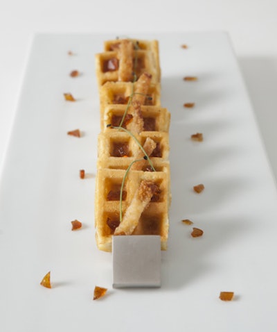 Waffle hors d’oeuvres infused with chicken, garnished with crispy chicken skin, chives, and syrup drizzle, by Canard Inc. in New York
