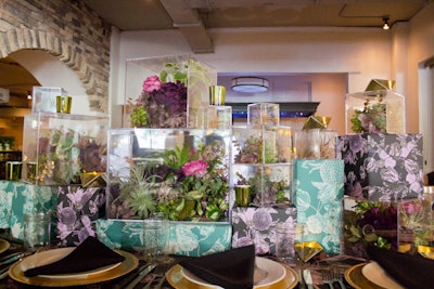 Flower and succulent arrangements in clear boxes sat atop deep teal and purple floral-wrapped boxes to form what designer Elizabeth Mollen from Stone Textile Studio called “modern garden party.”