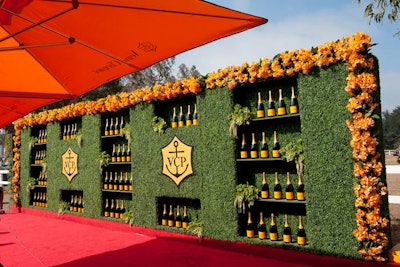 The press wall was made up of 36 feet of faux hedging with recessed bottle shelves, a pair of logos, and a 56-foot-long border of silk flowers.