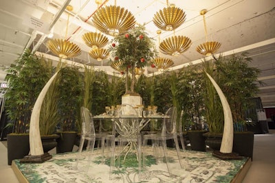 Golden palm-frond-inspired fixtures hung above the Garden of Eve-theme Circa Lighting display, which was designed by Sarah Whit Interior Design. The vignette also featured an apple tree centerpiece, animal-printed rug, and greenery as makeshift walls.