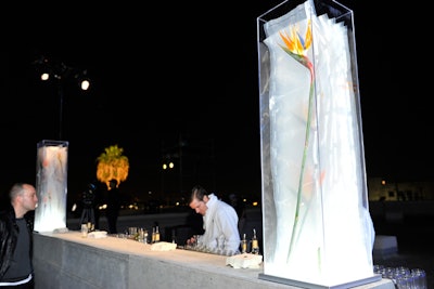 Eric Buterbaugh Flower Design created four main arrangements—two towering on each bar—that featured birds of paradise vacuum-packed and displayed in plexiglass light boxes. Vanda orchids, calla lilies, and anthurium were also displayed on tables to complement the event's stark, cement-abundant appearance and also vacuum-packed for an added survivalist effect.