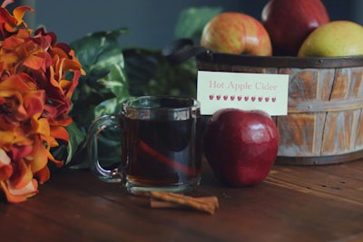 Hot apple cider with spiced rum, garnished with apple slices, cranberries, cloves, and cinnamon sticks for stirring, by Paramount Events in Chicago