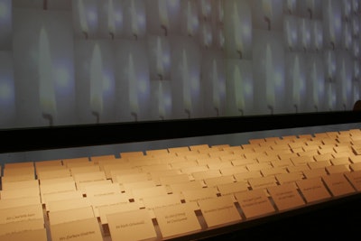 The gray theme of the Whitney's 2007 gala was also present at the entrance, where, in addition to a gray-carpet arrivals area, the color was represented by a large projection of candle flames shot against a pale gray background. The projection served as a dramatic backdrop for guests' name cards and supplied a soft light to the museum's entry hall.