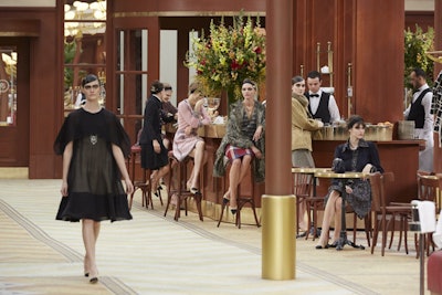 Models walked a runway that was, in fact, a printed canvas designed to mimic a traditional Parisian brasserie's immaculately tiled floor. While some models sat at specific booths, a host of others lingered by the bars.