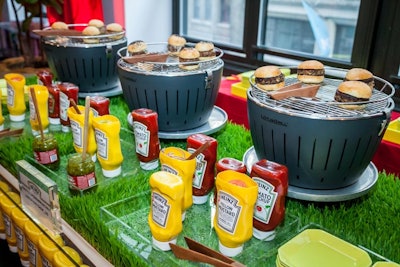 Guests could dress their burgers at a summer barbecue-style buffet table. Clear trays were placed on faux grass, and hollowed-out condiment bottles held tomatoes and onions.