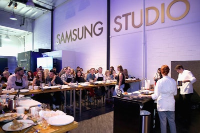 At the long-term pop-up Samsung Studio L.A., hosts Bill and Giuliana Rancic partnered with Top Chef's Marcel Vigneron to lead guests through a cooking experience. The chef used Samsung appliances in the pop-up kitchen for the cooking demo, and attendees followed along using appliances at their own long tables arranged classroom-style.