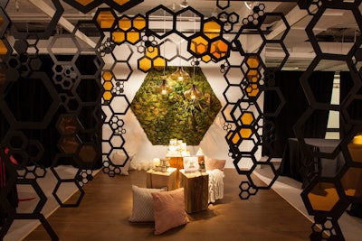 Inspired by honey, the vignette from Interior Investments by IA was surrounded by hanging fixtures with honeycomb patterns. The vignette also placed bottles of honey on wooden pedestals surrounded by pillows. A living green wall formed the backdrop.