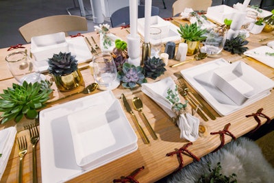 Red threads also appeared on the edges of a communal table designed by Perkins & Will and the Ruder Group. Like many of this year's tabletop settings, the design had a natural look. The table had no linens and was topped with succulents and white taper candles. Small sprigs of greenery were tied onto white napkins with twine, and a furry throw added texture to the seats.