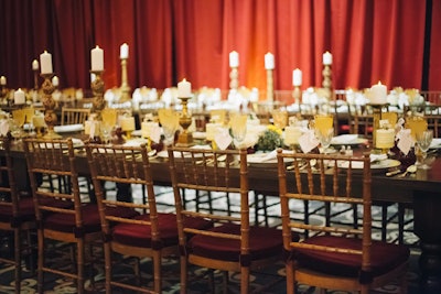 Revolution Event Design and Production used a rich color palette of deep red, gold, and yellow accents for the dinner tables. Centerpieces of greenery and tall candles ran the length of the two tables.