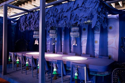 Sunbrella joined forces with Ghislaine Viñas Interior Design to offer a twist on a tropical tablescape by using a monochromatic purple-blue palette with hanging leaf-like fabric cutouts, banana-decorated fixtures, and tassel-adorned chairs.