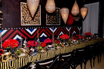 The Architectural Digest installation, designed by Bronson van Wyck, featured a custom-printed backdrop, a bold gold-and-black linen tablecloth by Larsen, earthy light fixtures by Tucker Robbins, and bright red floral arrangements.