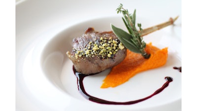 A lamb chop on a bed of orange, carrot, and ginger puree, blackberry demi and pistachio dust