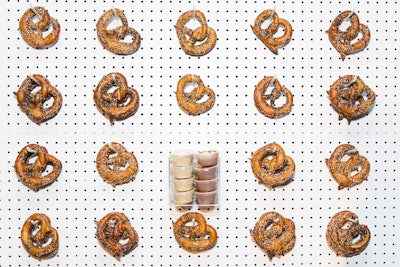 For the launch of the catering and event program at New York’s WTC860 - Riviera at the World Trade event space in December 2015, Riviera Caterers built a 24-foot-long, 8-foot-high pretzel wall. The interactive wall held 600 pretzels of different flavors, including garlic parsley, cheddar, cinnamon, salted, and plain, along with dipping sauces. The setup is customizable and can be converted for a variety of displays such as a salad or bagel bar.