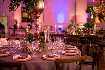 Wooden chairs in a rustic style contrasted with tabletops punctuated by refined golden details like taper candle holders and anemone-like objects.