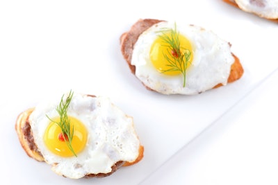 Sliced tenderloin, sunny-side quail egg, and white truffle oil on a crostini, by Puff ‘n Stuff Catering in Orlando