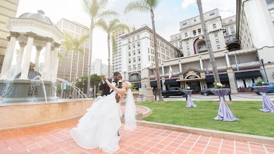 A bride and groom pose in front of the Broadway Fountain and U.S. Grant Hotel
