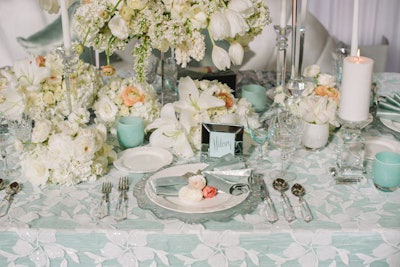 “The Iridescent Allure” table, designed by Hilary Hamer and Commerce Flowers, had a feminine look in pale blue and white with an overall floral motif. Details included mirrored seating cards, taper candles, and crystal glasses and candlesticks.