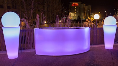 Illuminated glow spheres, planters, and a curved bar for an outdoor event.