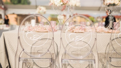 A custom-printed monogram on acrylic chairs for an outdoor tented wedding.