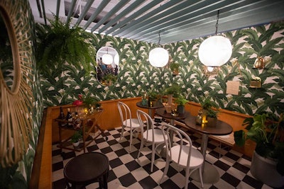 Interior Investments' booth was designed by Partners By Design. The space was meant to evoke a cafe in Havana, and featured wallpaper printed with palm leaves. Some guests ducked into the space during the opening-night 'Cocktails by Design' event, and had snacks and drinks at the low-top tables.