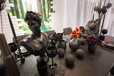 One of Modern Luxury Interiors Chicago's tables was designed by Casa Sapzio with SuzAnn Kletizien Design. The nearly all-black decor comprised busts, glossy wine glasses, and stone balls. In the background, a white brick wall gave way to a painted forest view.